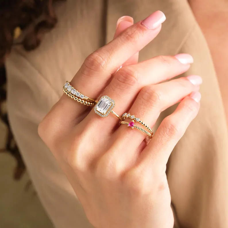 When it comes to engagement rings that combine sophistication with subtle radiance, emerald cut diamonds stand in a league of their own. Defined by their step-cut faceting and rectangular shape, emerald cut rings are admired for their clean lines, timeless elegance, and the soft, reflective glow that sets them apart from more traditional brilliant cuts. At KRK Jewels, the emerald cut is at the heart of many signature engagement ring styles. Rather than relying on intense sparkle, these step-cut stones offer a mirror-like brilliance—known as “step-cut brilliance”—that emphasizes clarity, symmetry, and grace. Each facet is strategically arranged to draw the eye into the stone’s depth, creating a quiet yet powerful impression. Designed to Highlight Elegance KRK’s emerald cut ring styles are crafted to maximize the beauty of this unique faceting. From minimal solitaires to intricate halos, each design frames the step-cut diamond in a way that enhances its structure and sophistication. Minimalist solitaires emphasize the elongated shape and geometric charm of the emerald cut. Halo styles amplify the glow, using pavé diamonds to contrast with the center stone’s clean surface. Three-stone rings, with baguette or trapezoid accents, create linear harmony and symbolic meaning. East-west settings turn tradition sideways, offering a sleek, contemporary edge to the classic shape. More Than a Cut—A Statement Step-cut brilliance is not about flash—it’s about clarity. Brides drawn to emerald cuts often appreciate the honesty and depth symbolized by the cut. These rings reflect a relationship built on transparency and trust. The bold, open facets are unforgiving of flaws, making the emerald cut a celebration of natural beauty and precision craftsmanship. Crafted with Purpose at KRK Jewels KRK Jewels hand-selects each emerald cut diamond, prioritizing clarity and proportion—essential qualities for showcasing the step-cut’s reflective power. Skilled artisans then create settings that complement and elevate the stone without overwhelming it. Clients can choose from lab-grown or natural diamonds, select from multiple metals, and personalize every element of their ring. Whether classic or contemporary, each piece is made to reflect the wearer’s style and story. Emerald cut engagement ring